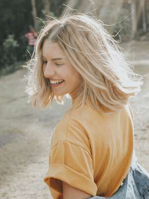 Woman in mustard t-shirt smiling under the lights of a sun.