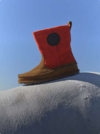 Brown boots, blue jeans and knitwear lying on white ground.