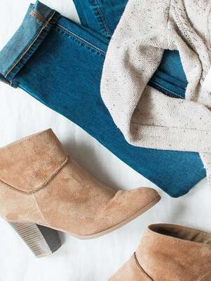 Brown boots, blue jeans and knitwear lying on white ground.